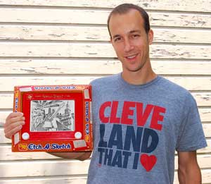 George Vlosich III holds an Etch a Sketch drawing he made of various Cleveland landmarks. He wears a graphic T-shirt designed by the art company he ow