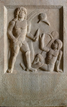 This 1,800-year-old tombstone depicts a gladiator holding two swords standing above his defeated opponent who is signaling submission. The inscription